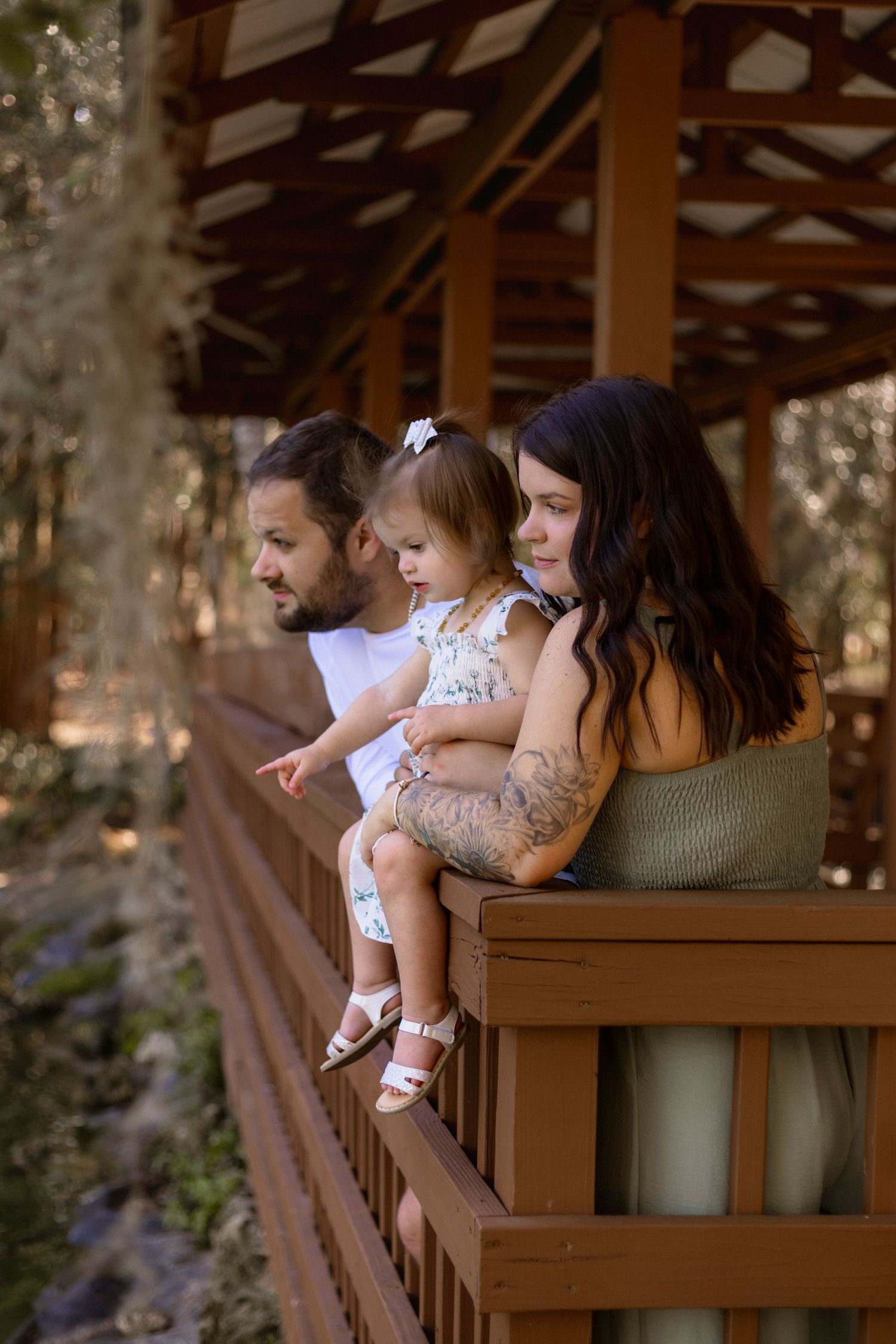 A family of three, mother, father and young daughter looking out to a lake. Girl is pointing while parents are looking ahead.