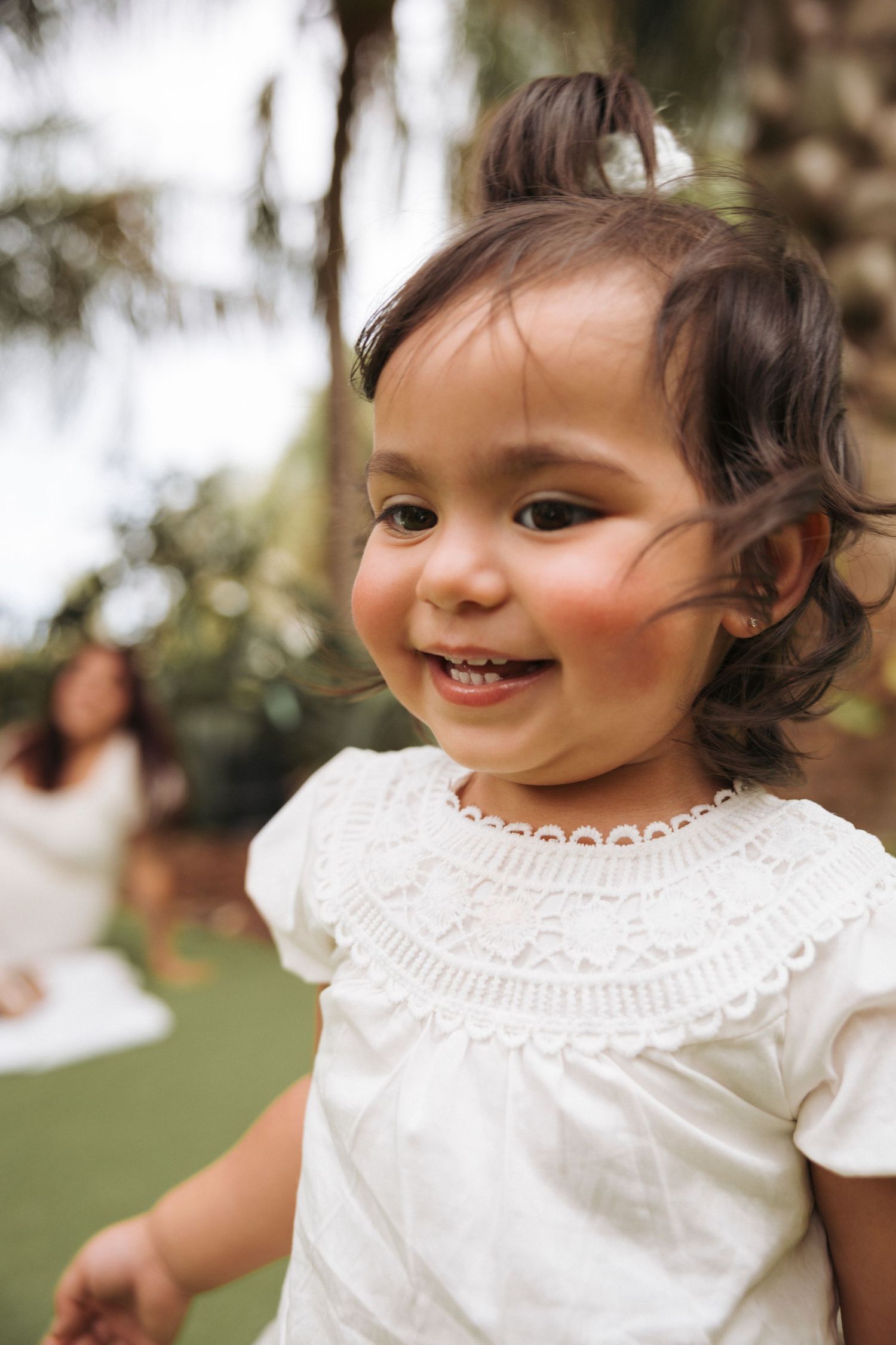Close up portrait of a toddler smiling seemingly running away while her pregnant mother is blurred in the background.
