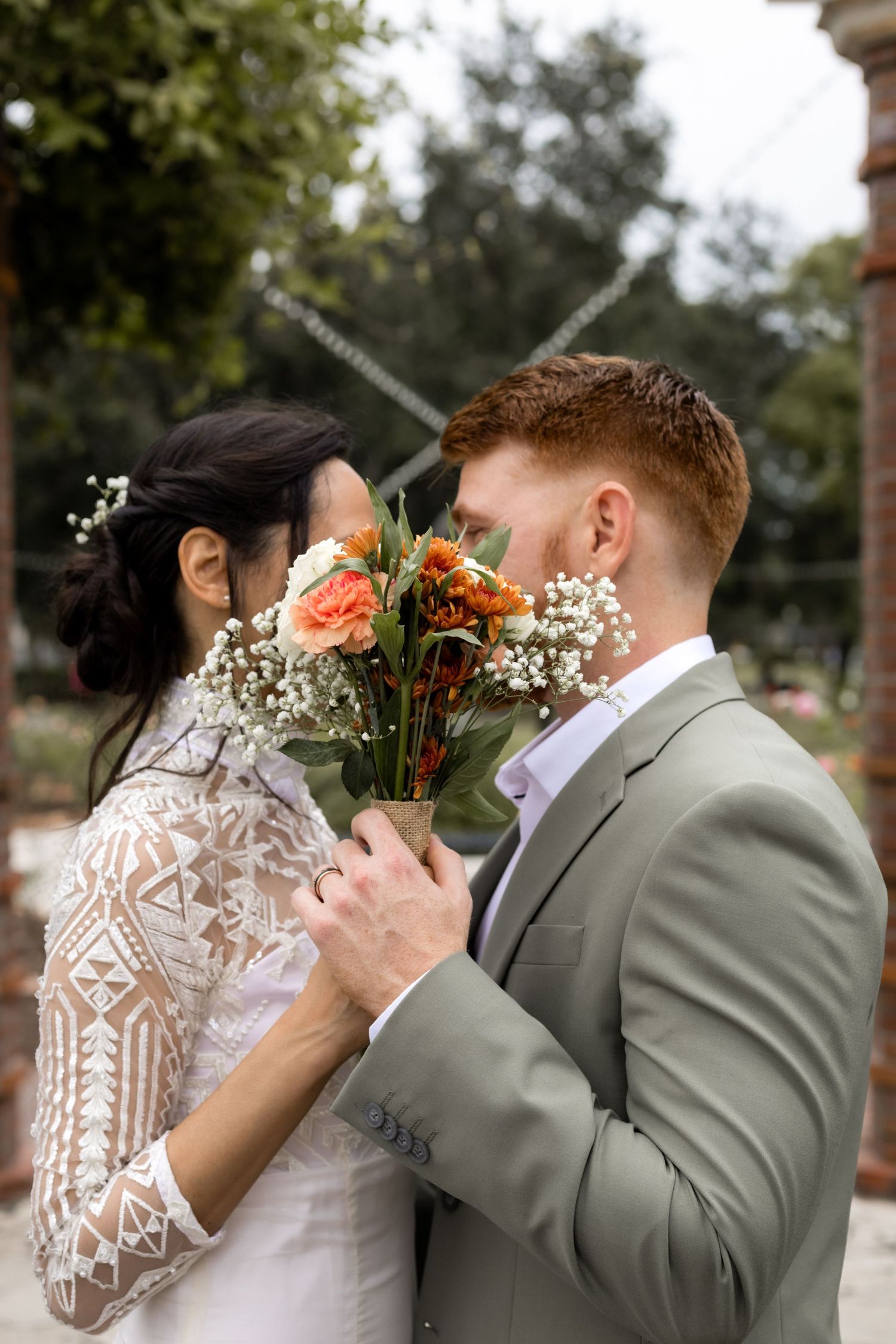 Young couple colorful and vibrant portrait of their wedding. Bride and groom looking at each other but covering face with flowers in center.