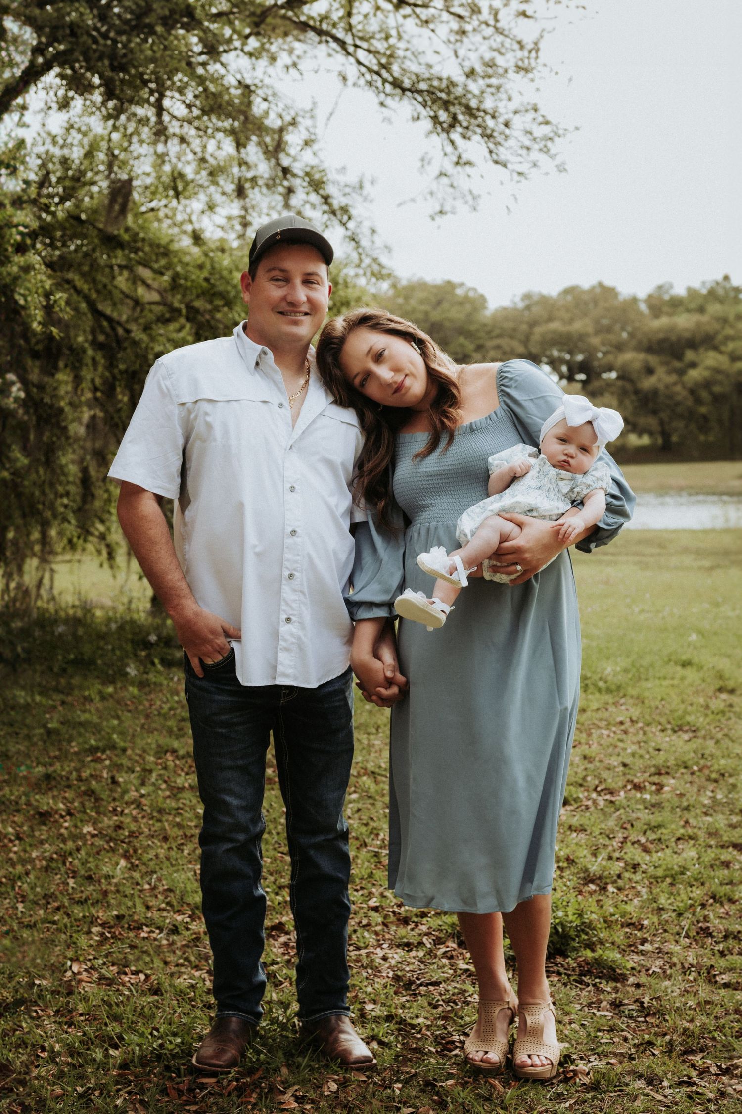 Portrait of family of three. Female is resting her head on her husband's shoulder as she is holding their baby.