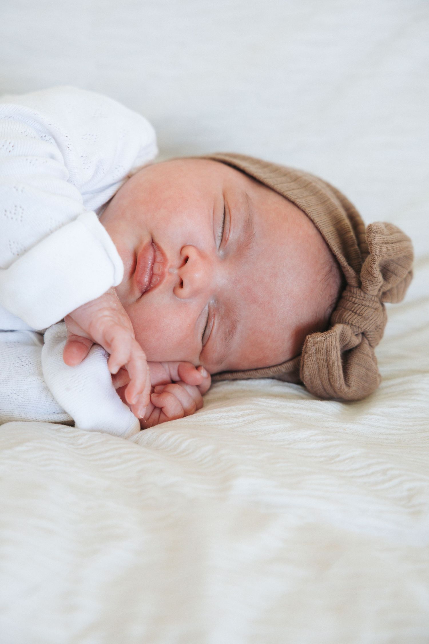 Close up portrait of a newborn in a white onesie wearing a brown bow in a studio-like setting.