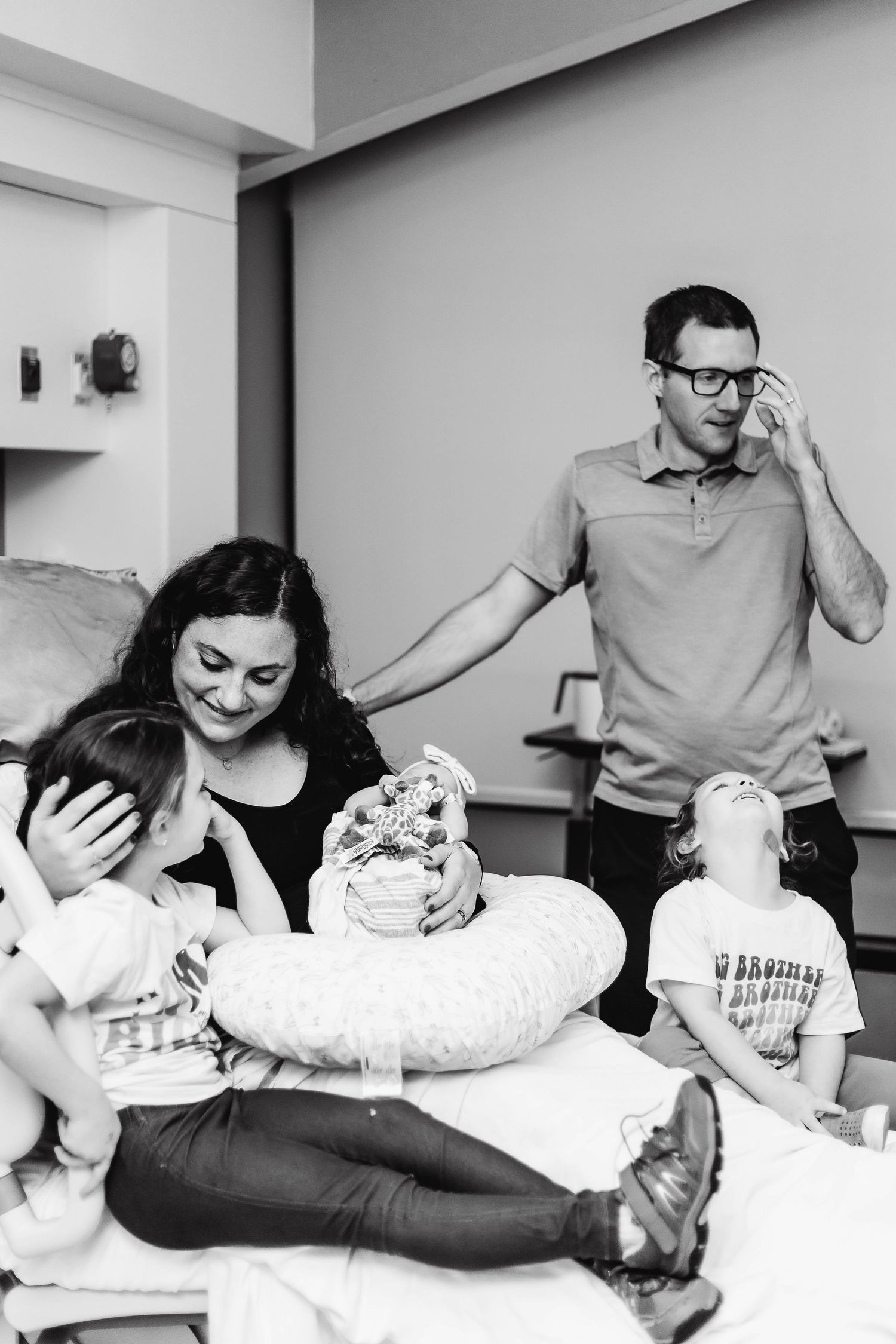 Family stands together after delivery. Mother cradles her oldest head while holding her newest addition, while middle child looks up at dad.