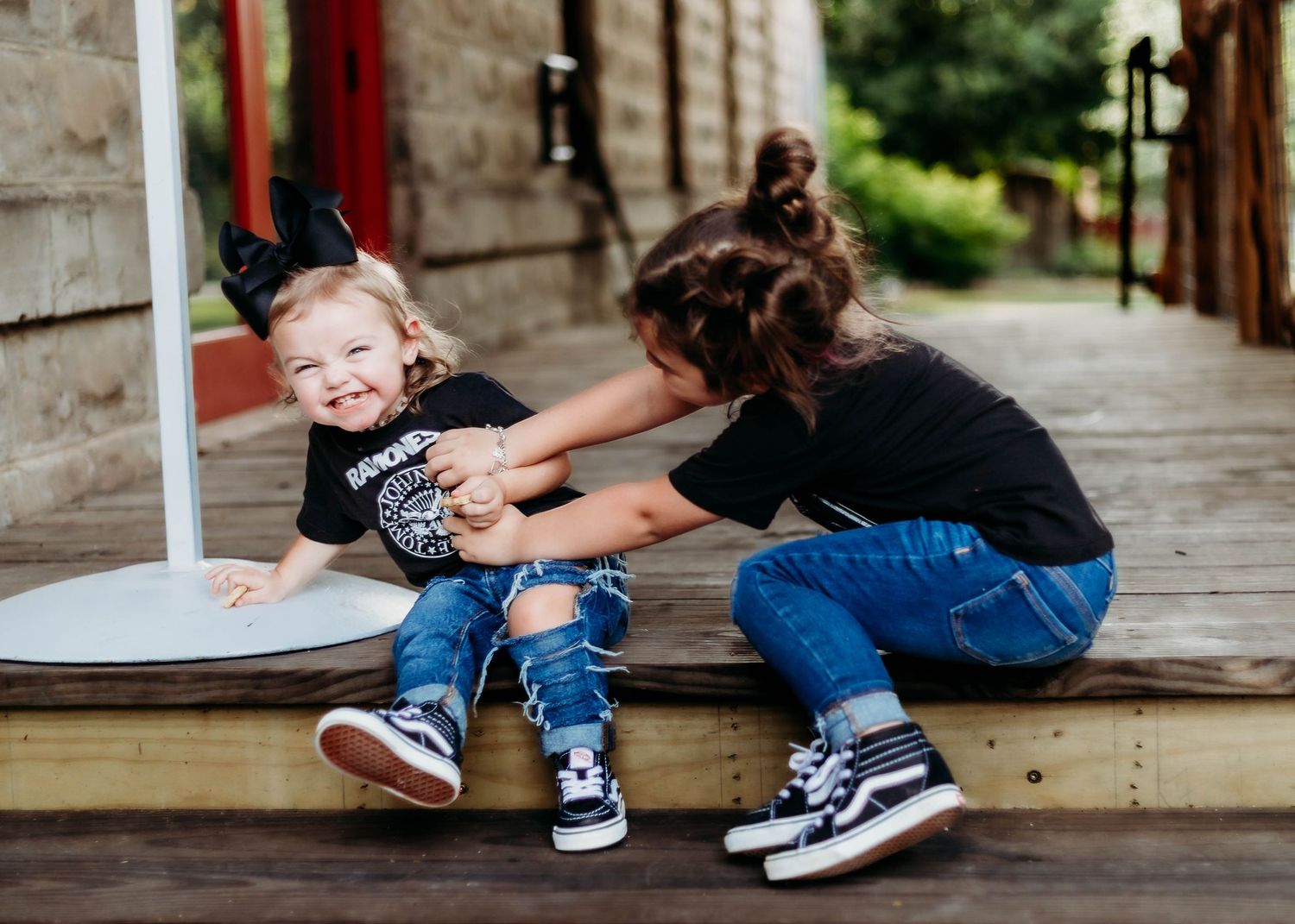 Older sister tickles little sister while sitting on steps of a deck