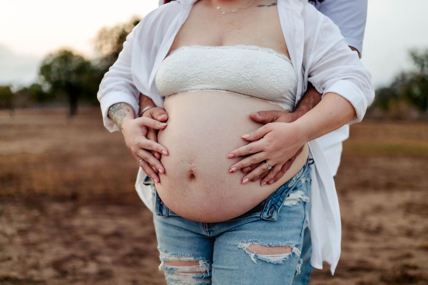 Husband and wife hold wife's pregnant belly during maternity session.