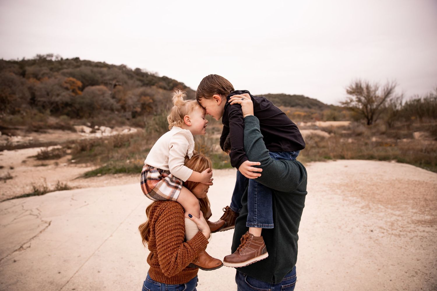Mother and Father have kids on their shoulders and kids touch their heads together.