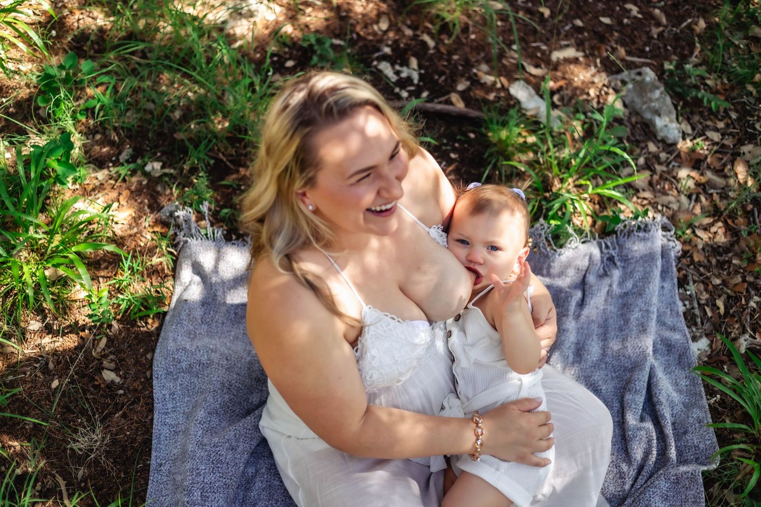 Mother laughs while nursing baby looks at camera