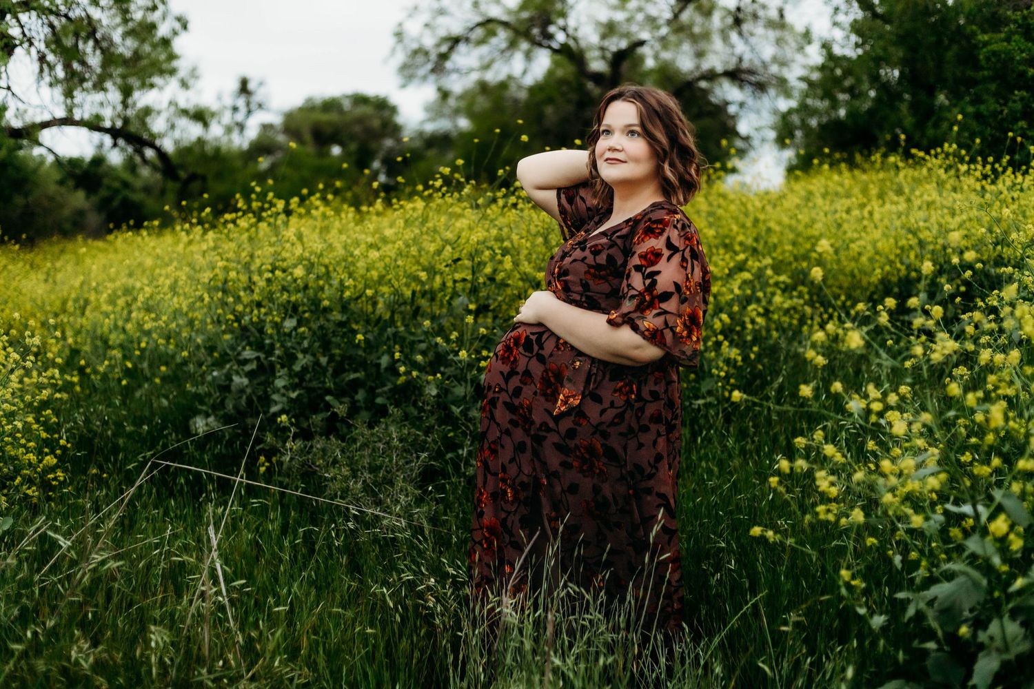 Pregnant mother poses in front of little yellow flowers