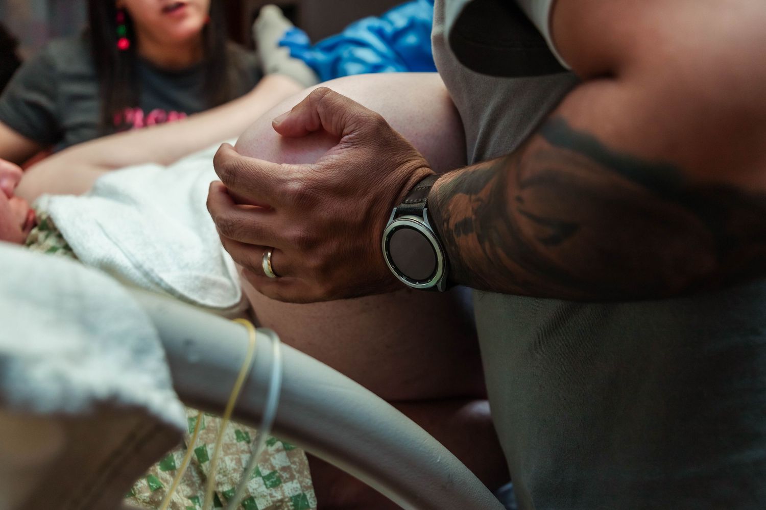 Husband holds wife's leg while she bears down to deliver their baby.