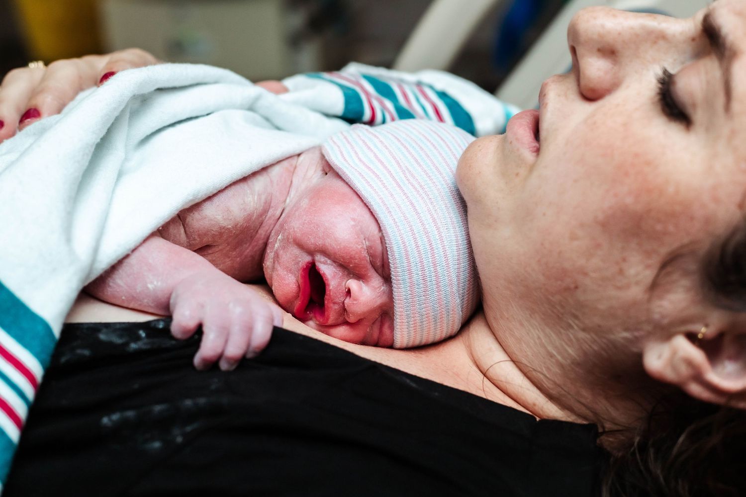 Mother holds newborn baby in hospital bed while baby cries on her chest