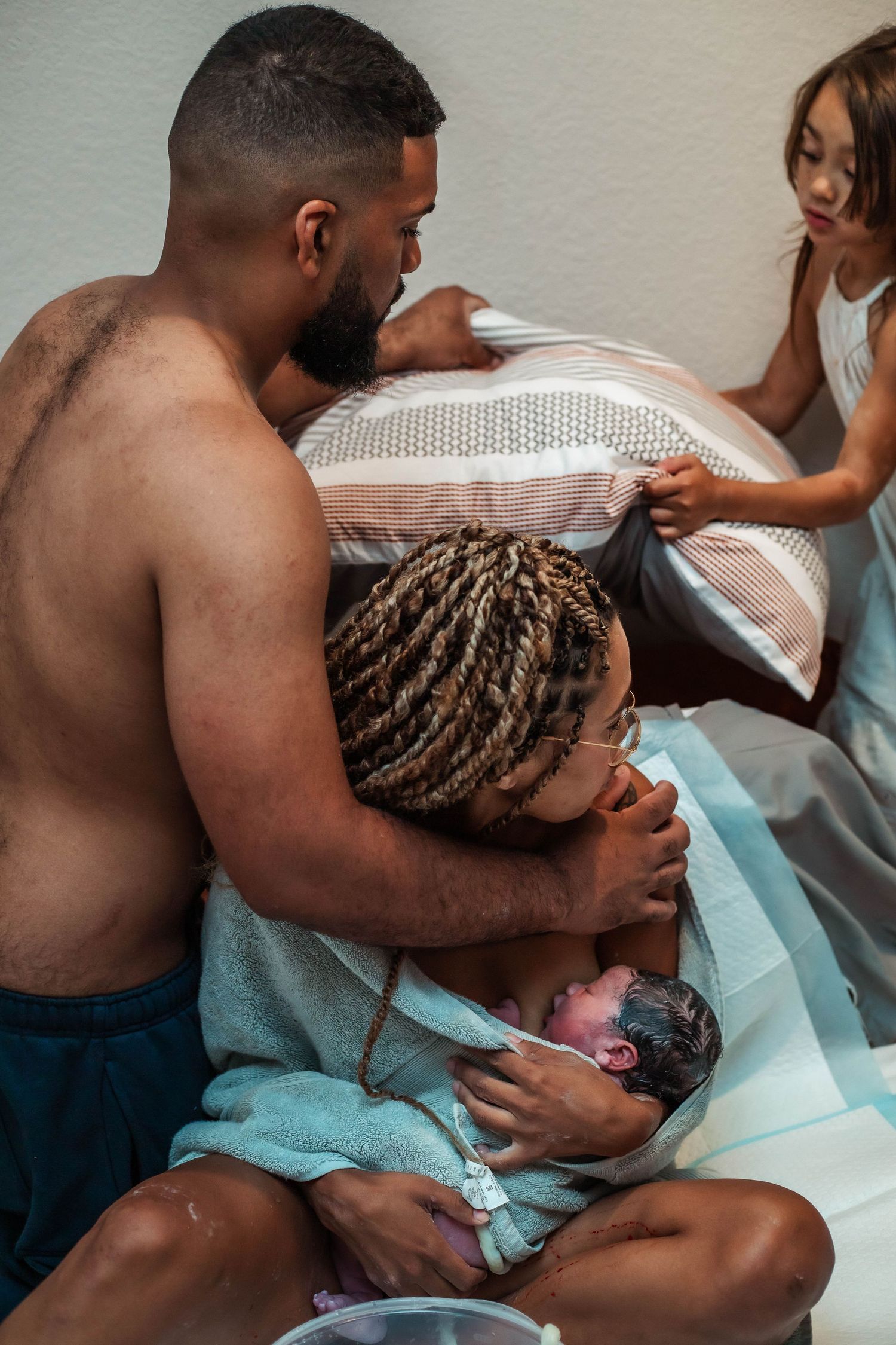 Husband and daughter help mother get comfortable in bed after homebirth