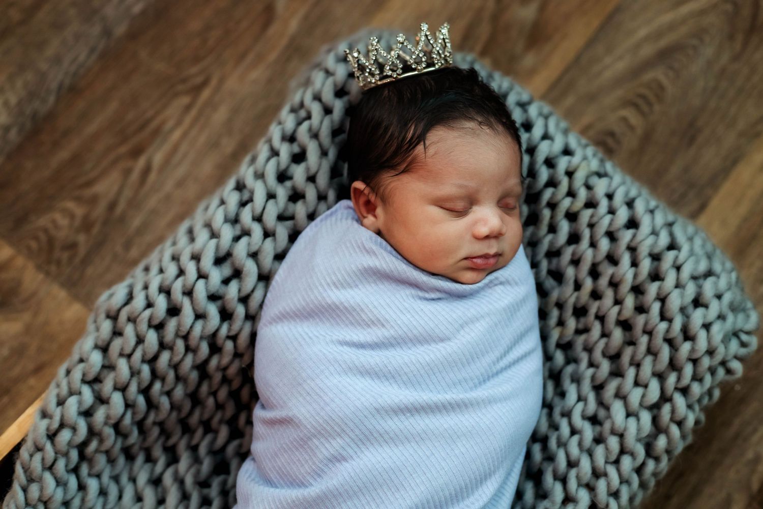Newborn baby girl wrapped in a purple wrap laying in a basket with a crown on her head