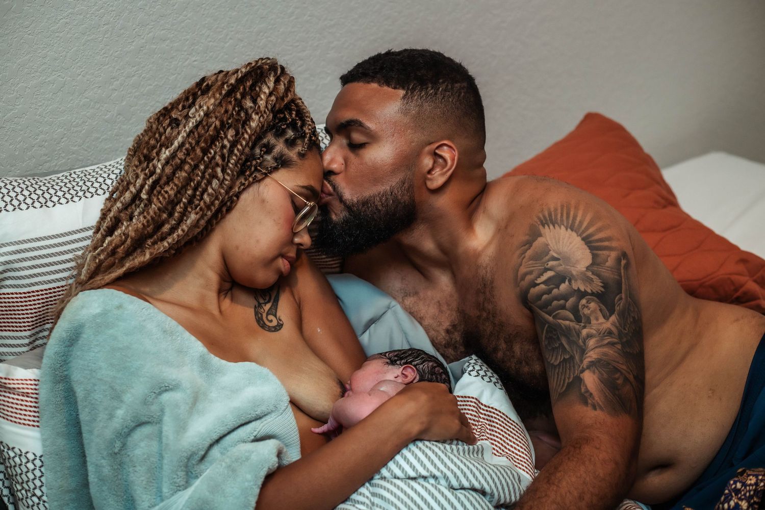 Husband kisses wife's head while she nurses newly born baby