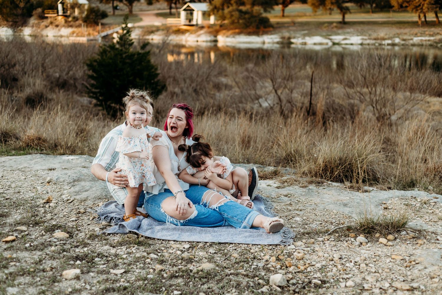Family sits on ground during their family session oldest daughter play bites moms forearm, while mom makes a surprised face
