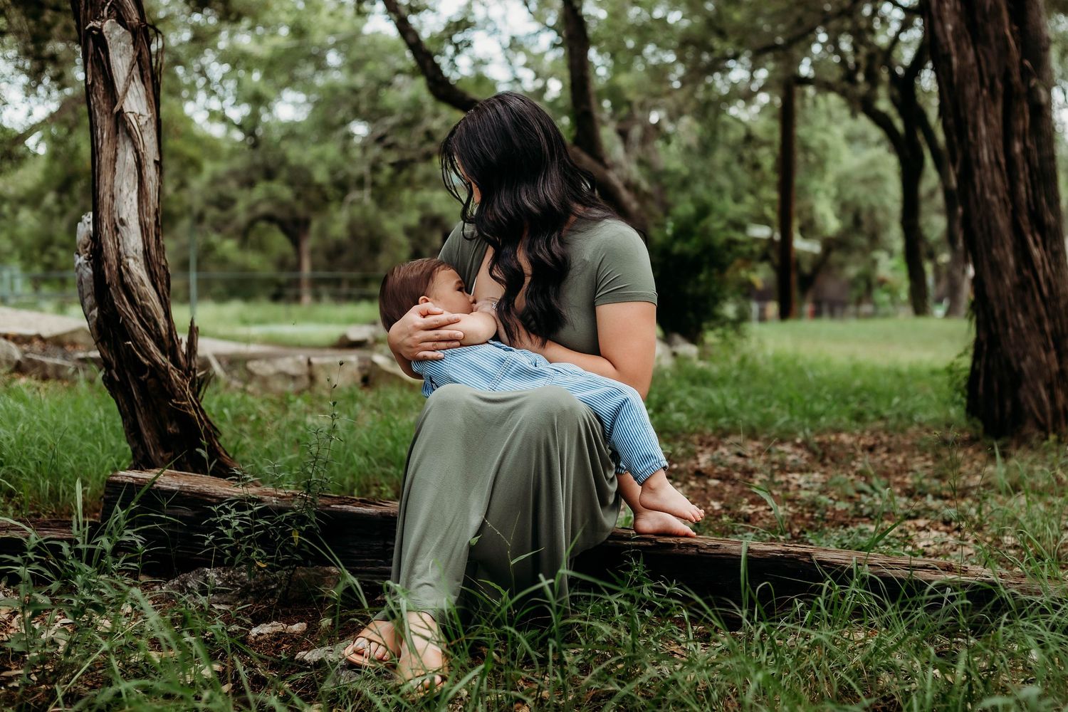 mother nurses toddler sitting on log outside