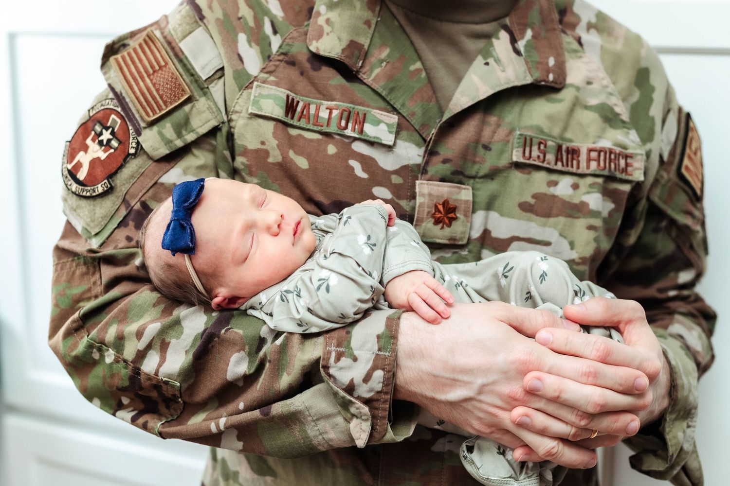 Air Force Officer holds his newborn daughter while wearing his uniform.