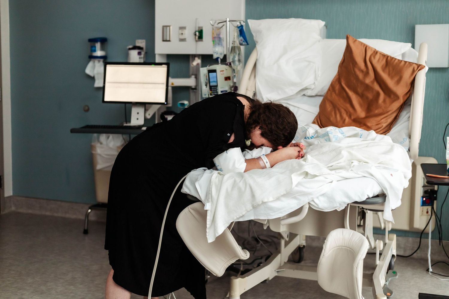 Laboring mother leans over hospital bed during contractions