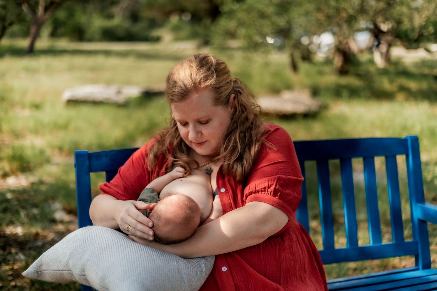 Mother nurses baby with pillow under her arm on bench