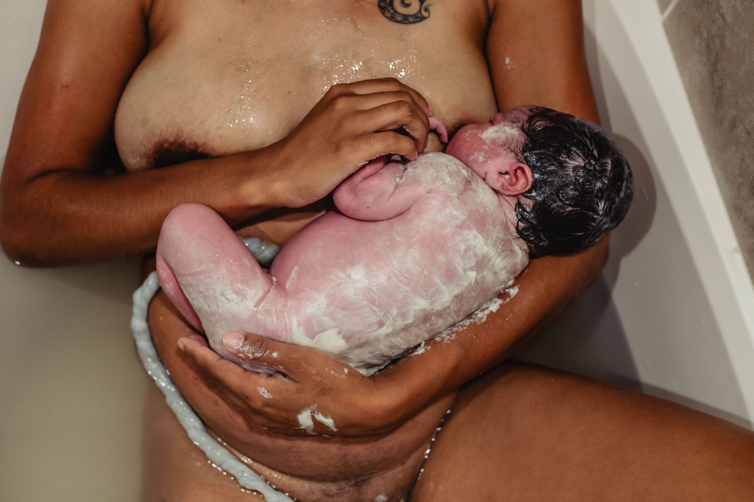 Mother holds baby to chest while nursing directly after birth