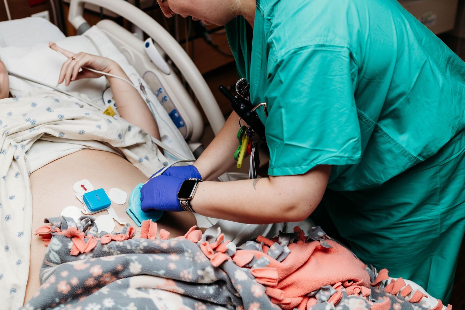 Nurse placing wired monitors on laboring mothers belly.