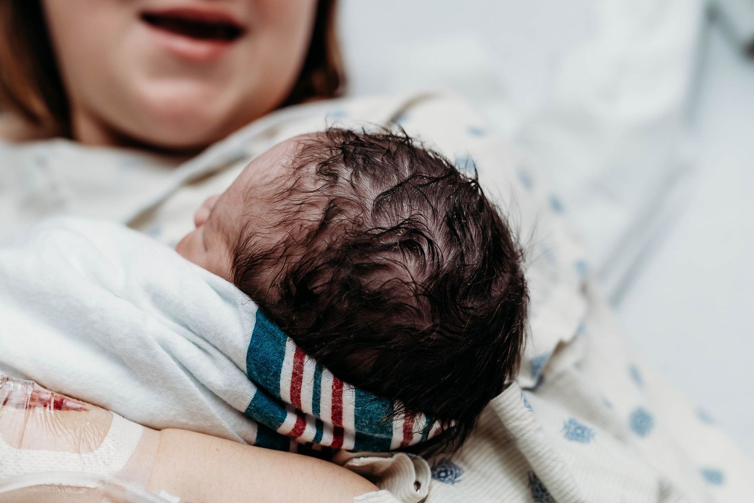 Mother talks to newborn baby, head is in focus with lots of hair