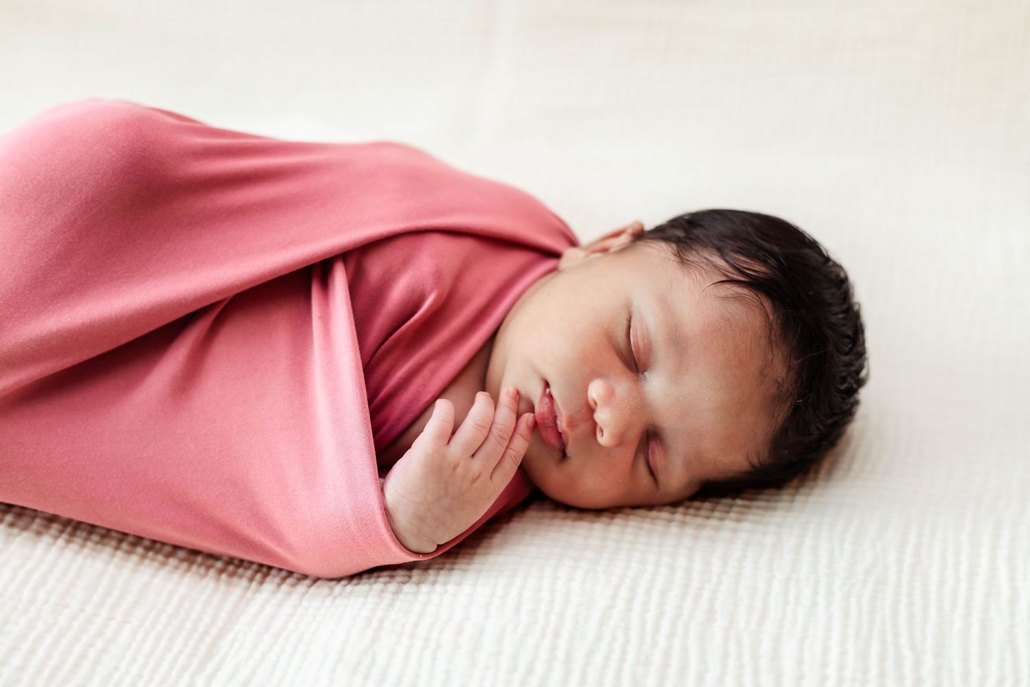 newborn baby wrapped in a pink wrap posing