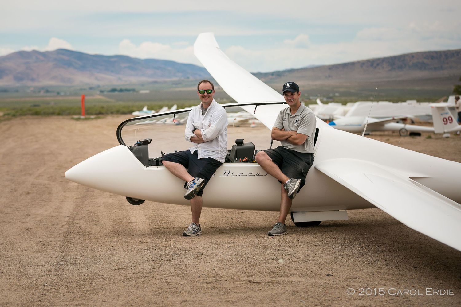 Two men sitting on the wing of a glider plane, smiling with arms crossed, ready for flight in Reno, NV.
