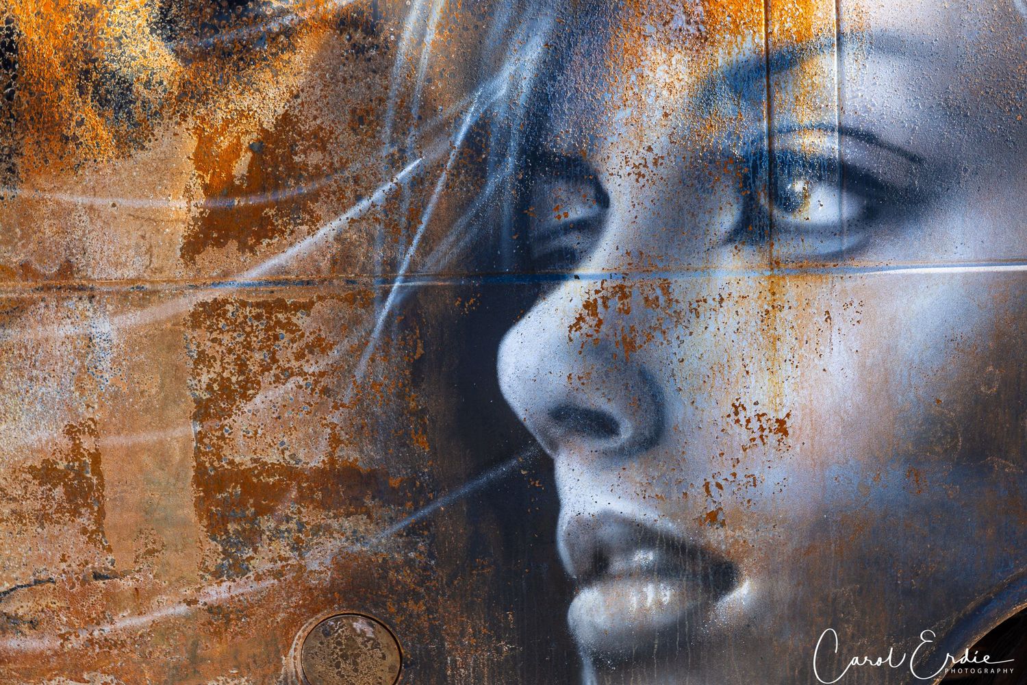 Graffiti art of a woman's face painted on rusted metal in Paradise, CA, blending urban decay and artistic beauty.