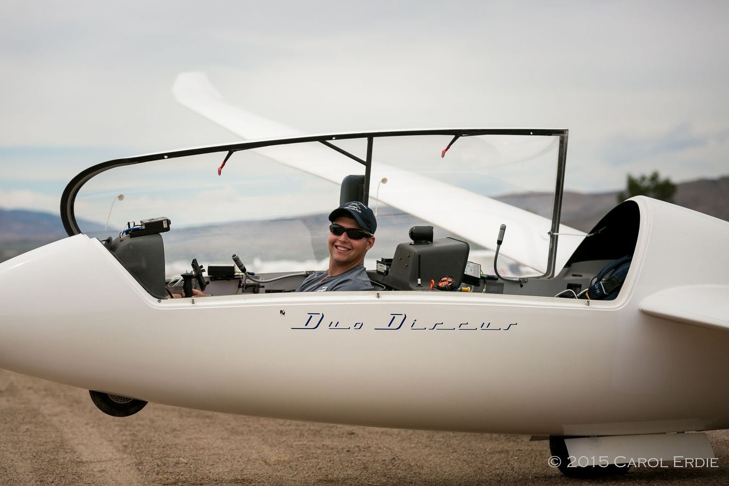 Man sitting in the cockpit of a glider plane, smiling and ready to fly, wearing sunglasses in Reno, NV.
