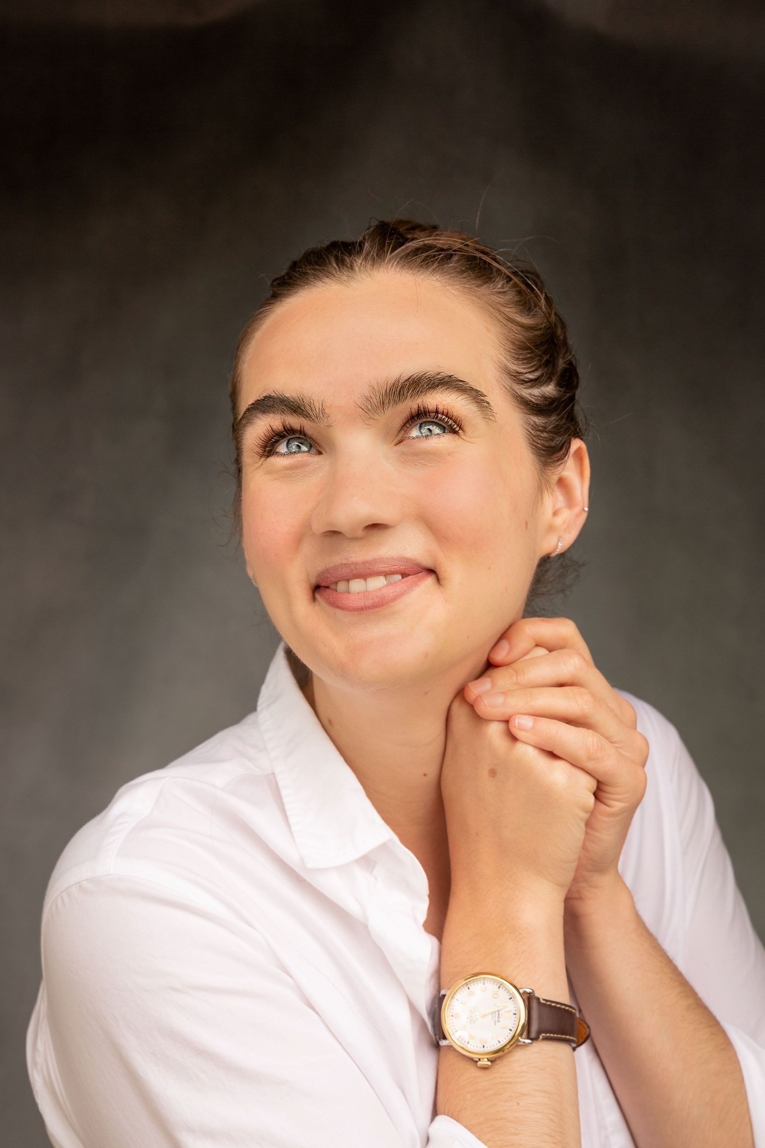 Woman in a white shirt smiling and looking upward, posing against a dark background in Half Moon Bay, CA.
