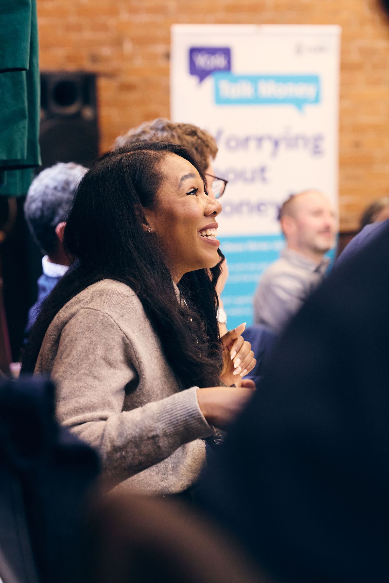 Smiling woman in glasses at a Talk Money financial wellness event, engaged in conversation with attendees.