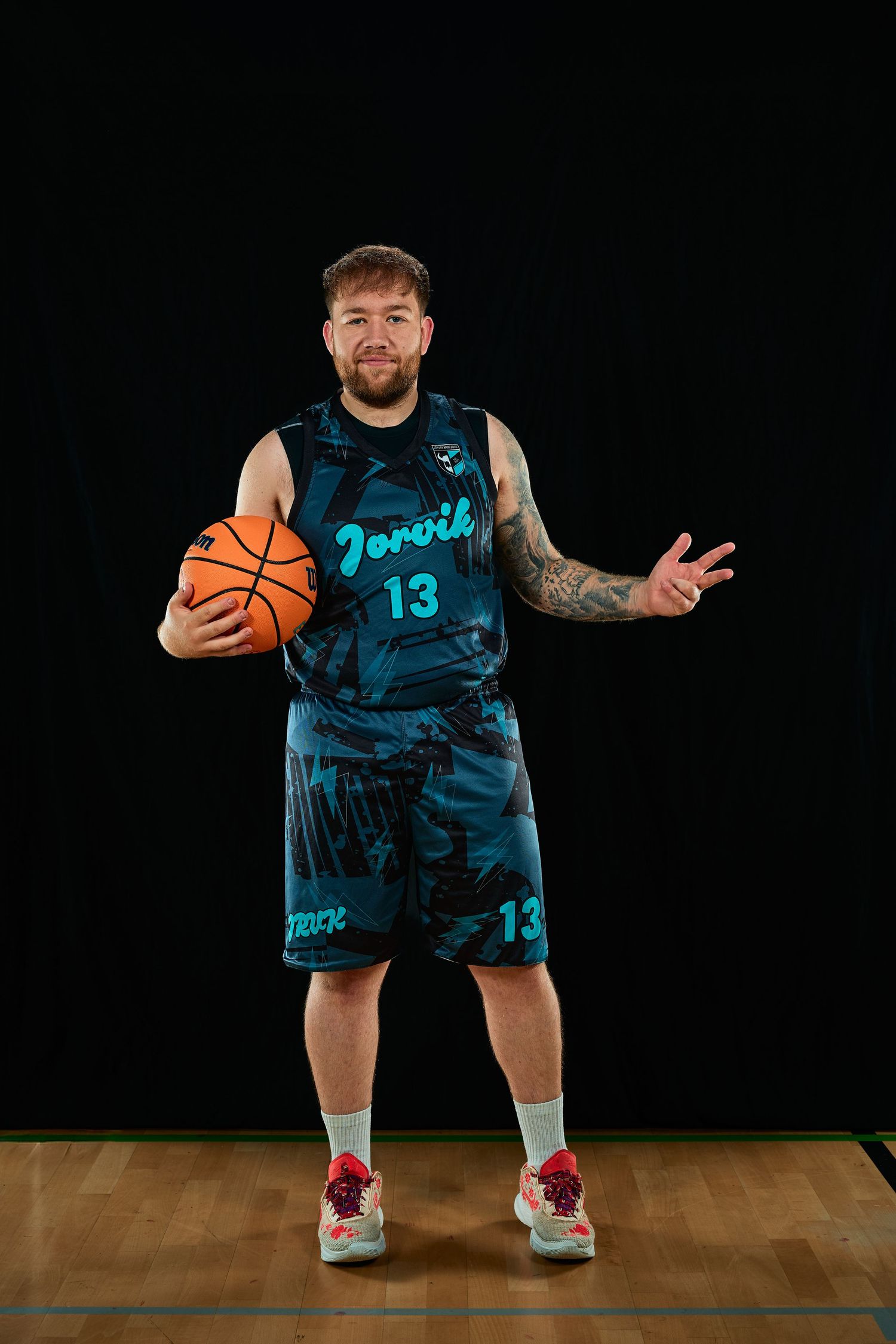 Player in blue basketball uniform demonstrating dribbling stance on wooden court.
