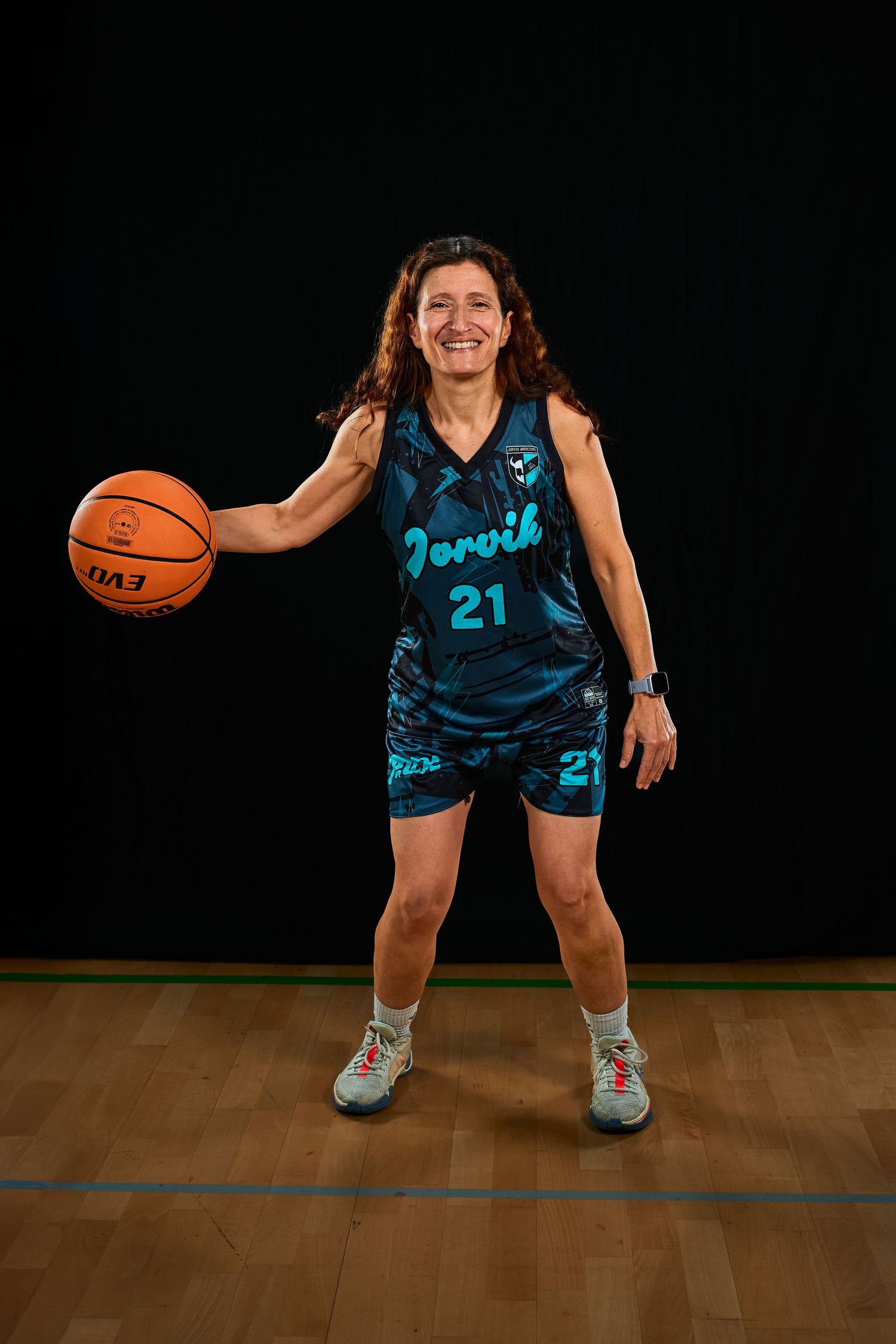 Basketball player in blue jersey demonstrating defensive stance on wooden court.