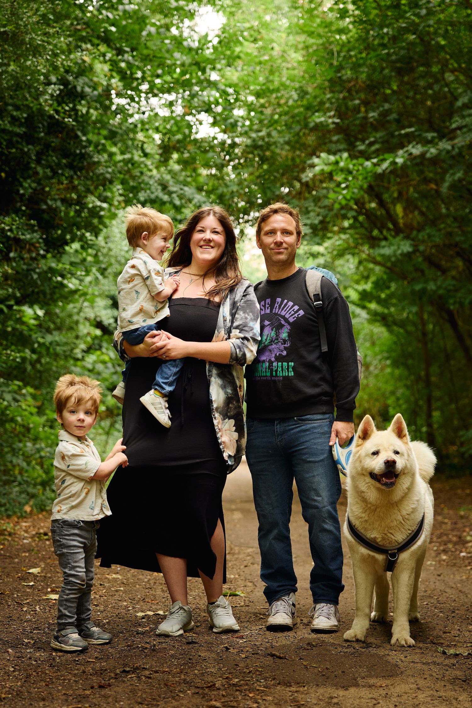 Family and white fluffy dog posing together on forest trail.