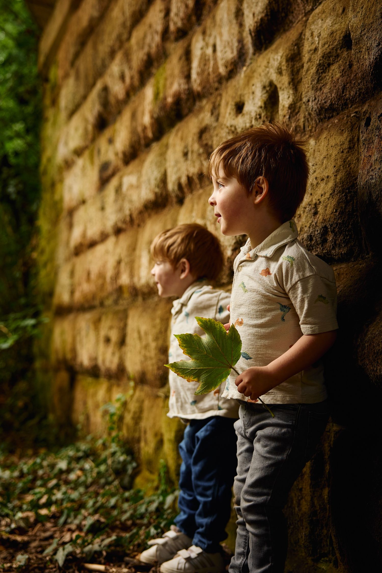 Two children lean against stone wall during outdoor portrait session.