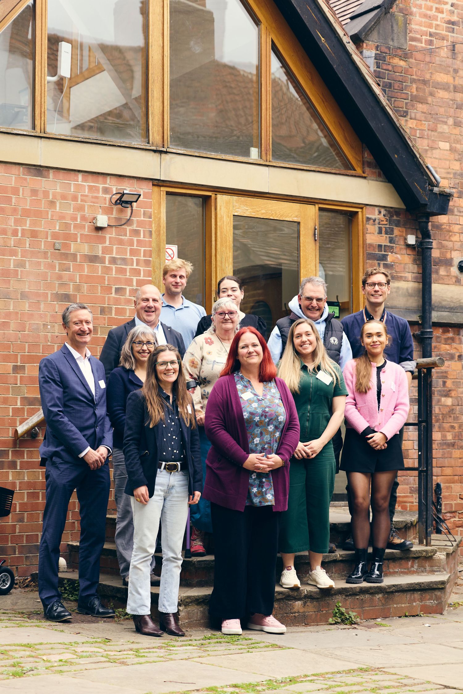 Group of professionals posing together outside a red brick building, smiling for a team photo.