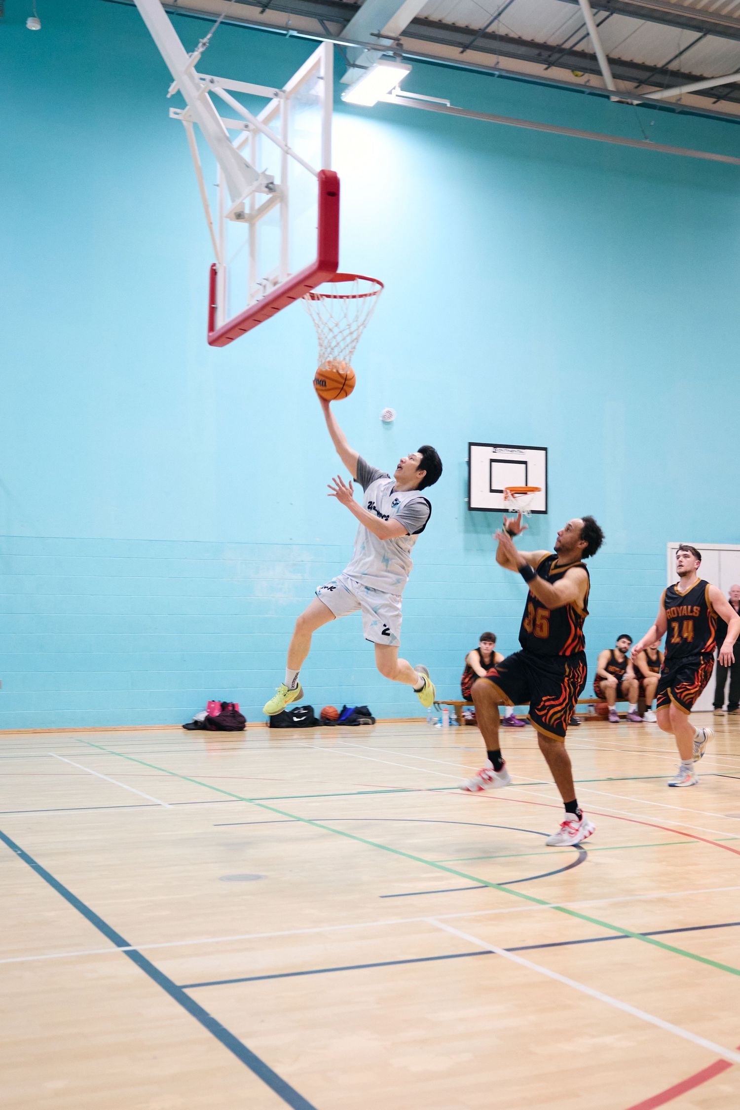 Basketball players compete for a rebound under the hoop during indoor game.