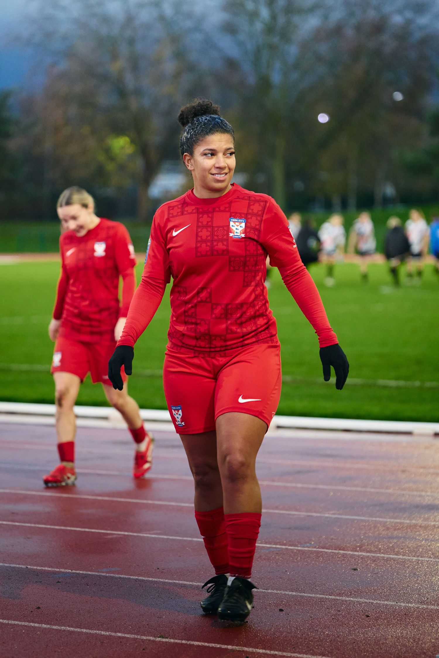 Athletes in red uniforms practice running drills on an outdoor track during training.
