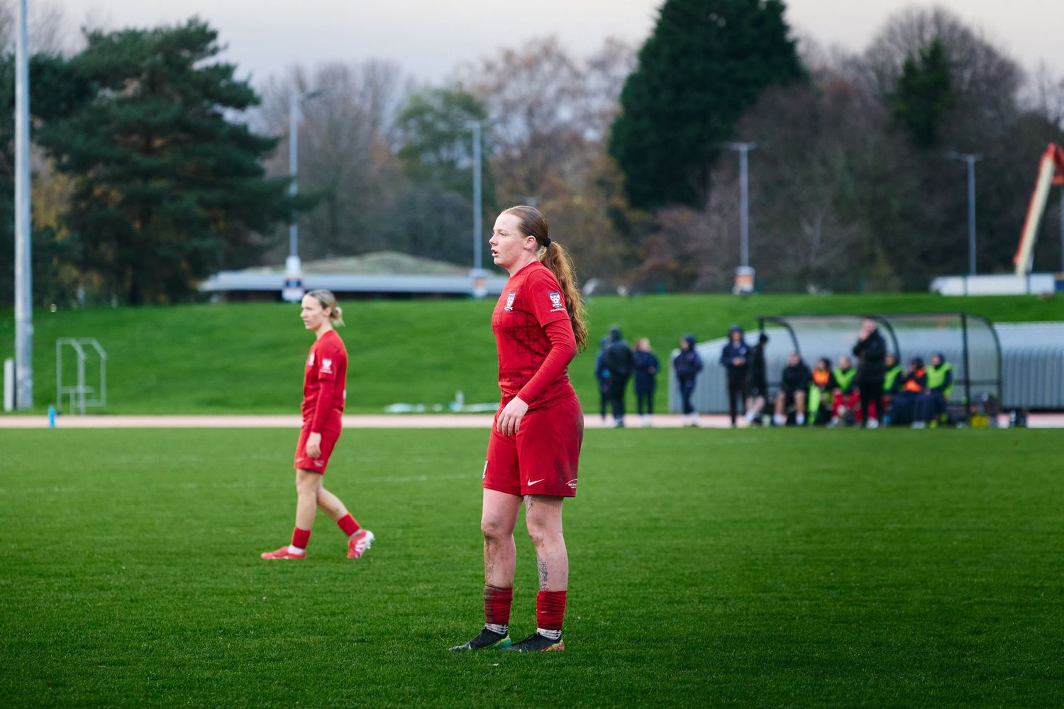 Soccer players in red uniforms stand on a green grass field during practice or training session.