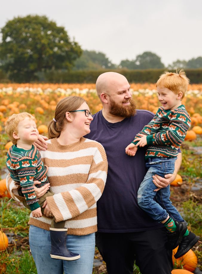 A family enjoying autumn moments together in a pumpkin patch wearing cozy sweaters.