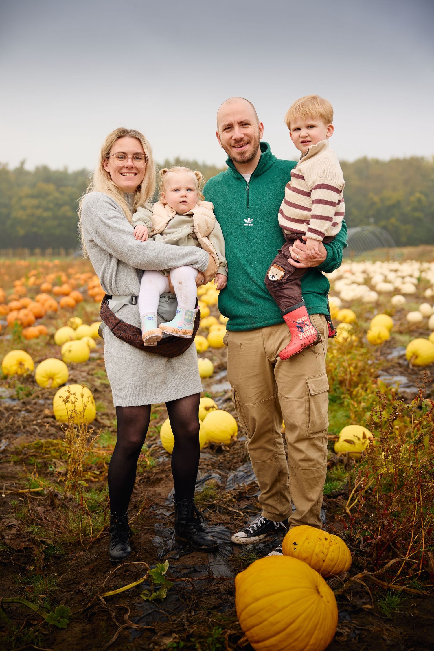 Family poses together in a golden pumpkin field during autumn harvest season.