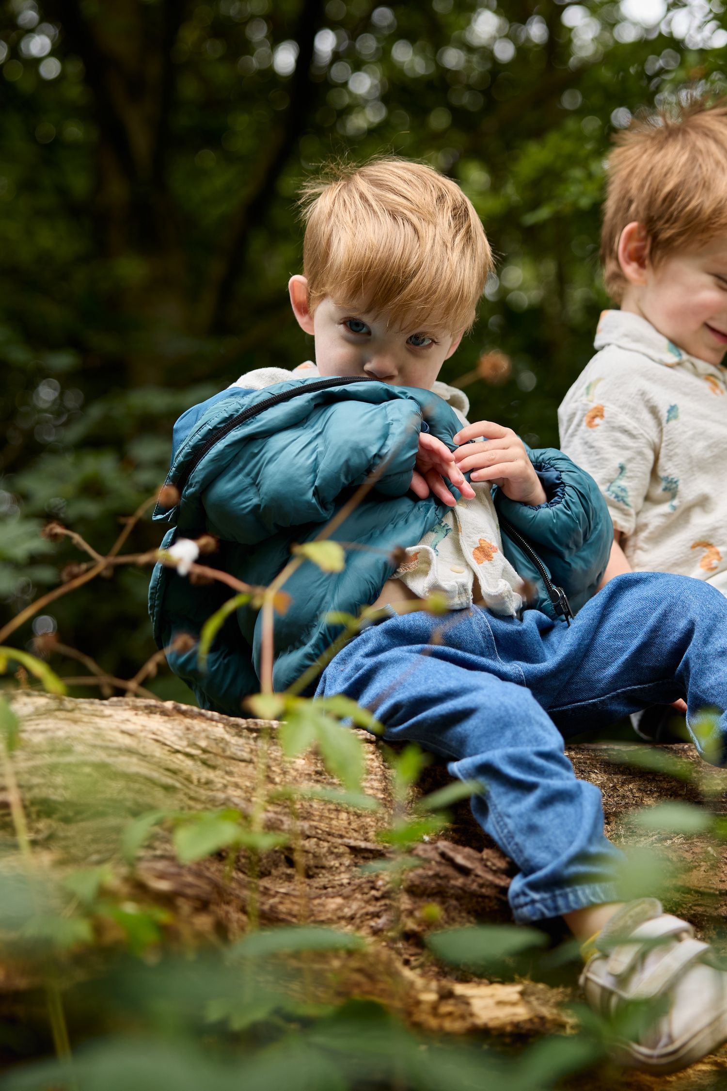 Child lying on forest ground exploring nature in casual outdoor wear.