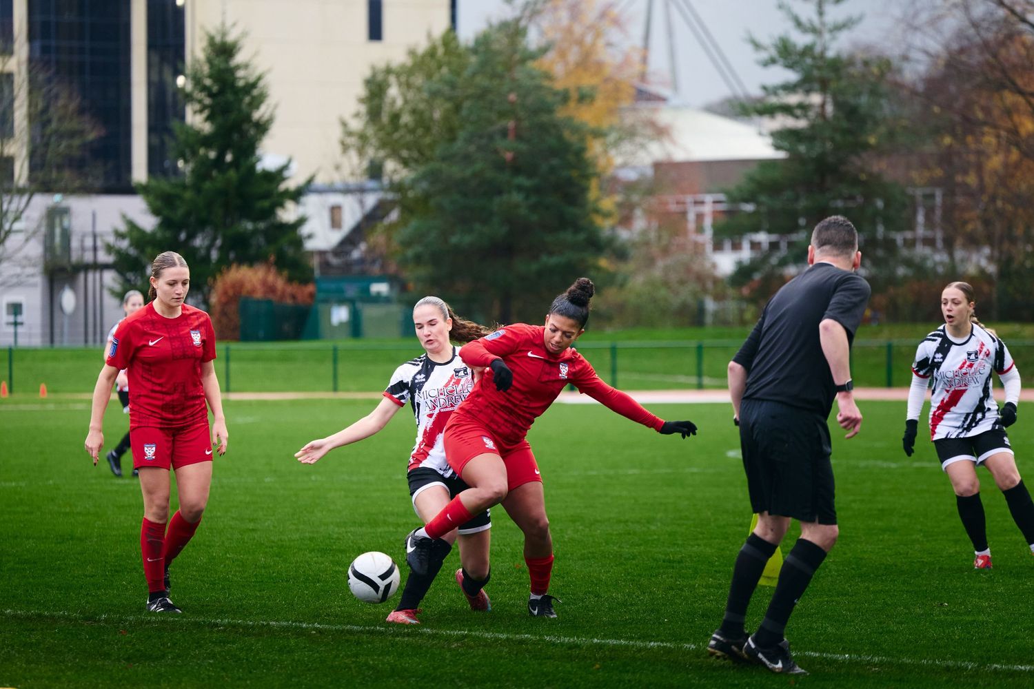 Soccer players in red and black-and-white striped uniforms compete for the ball during a match on a grass field.