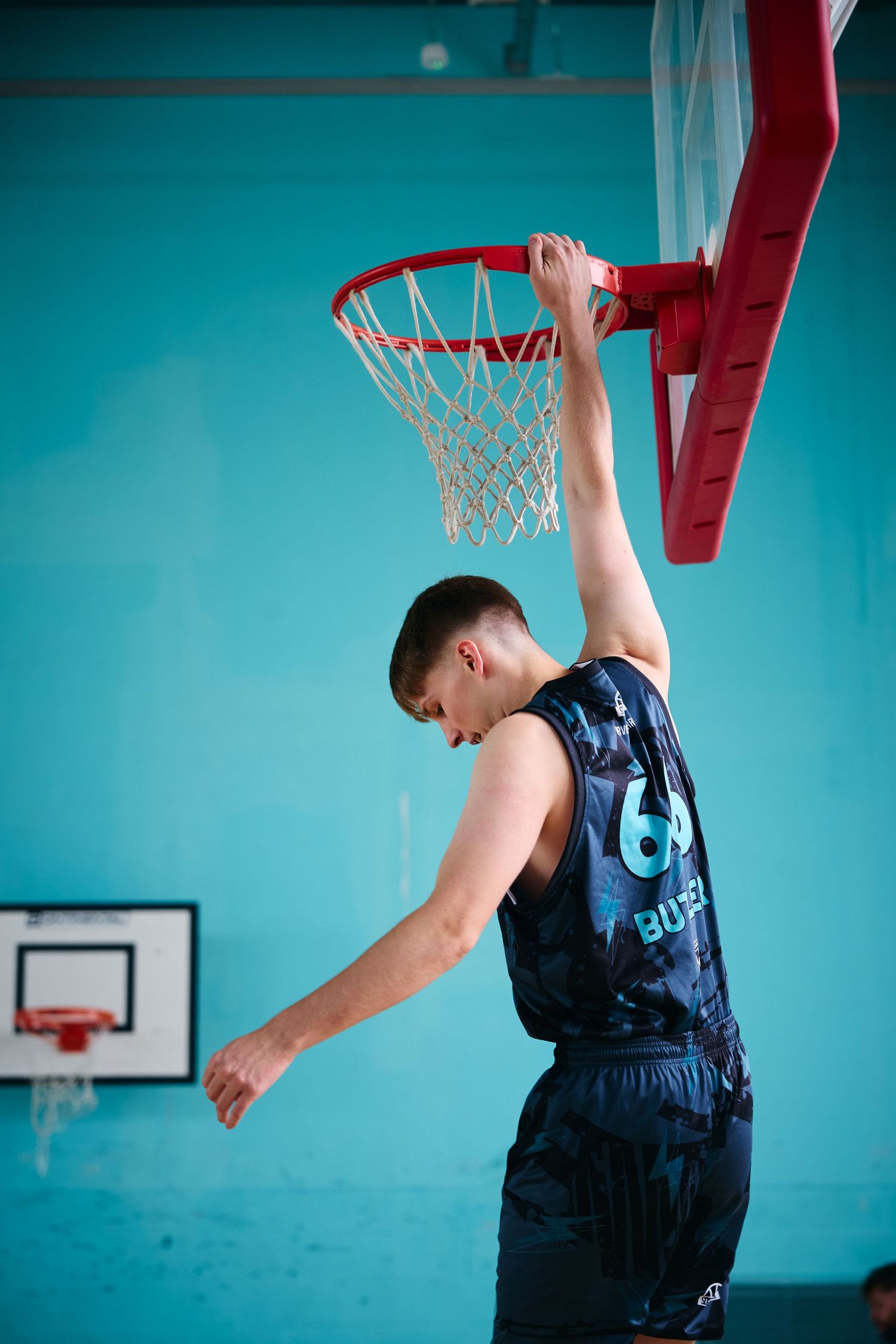 Basketball player in navy jersey performing jump shots against turquoise wall background.