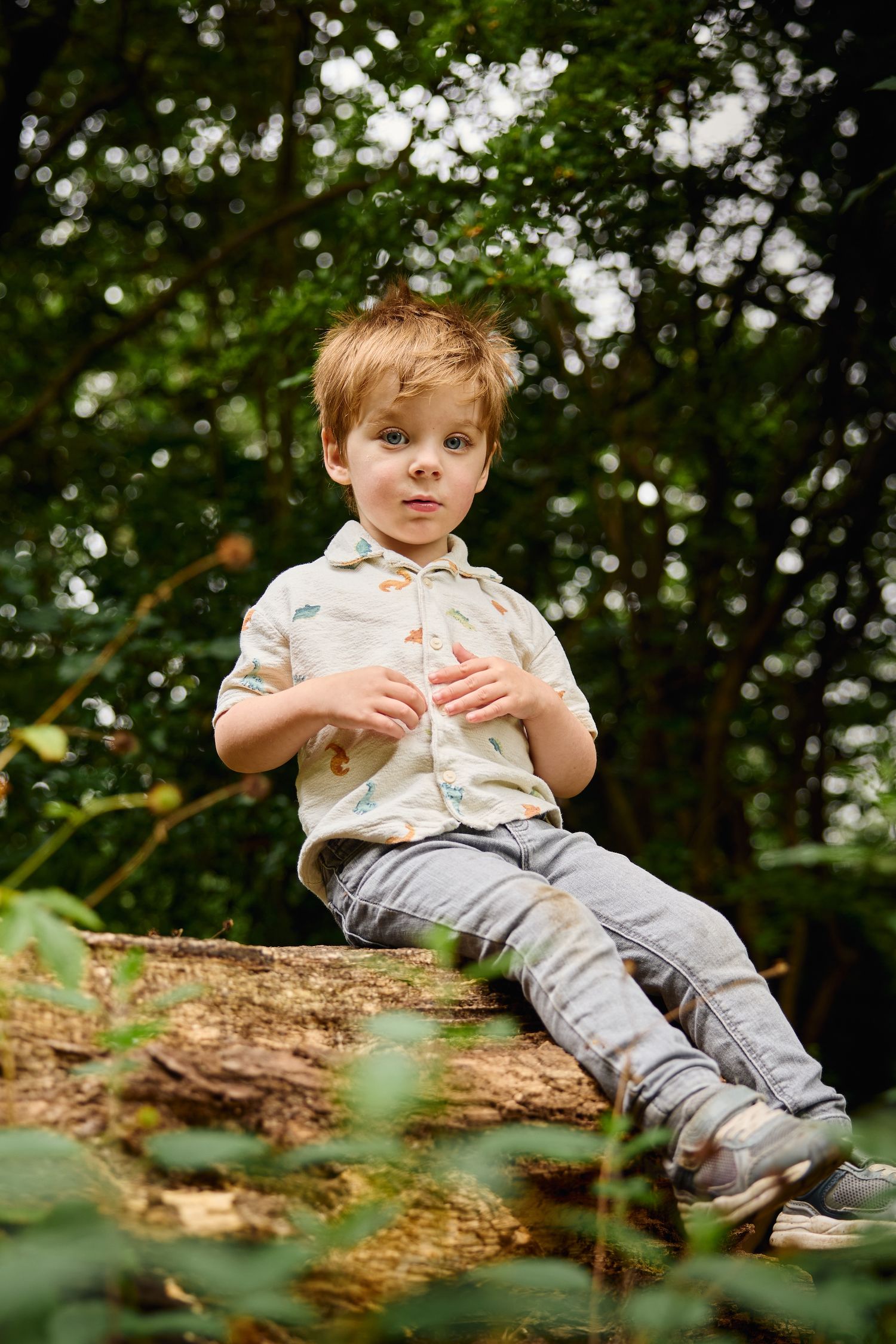 Child sitting on fallen log in forest wearing light colored shirt and jeans.