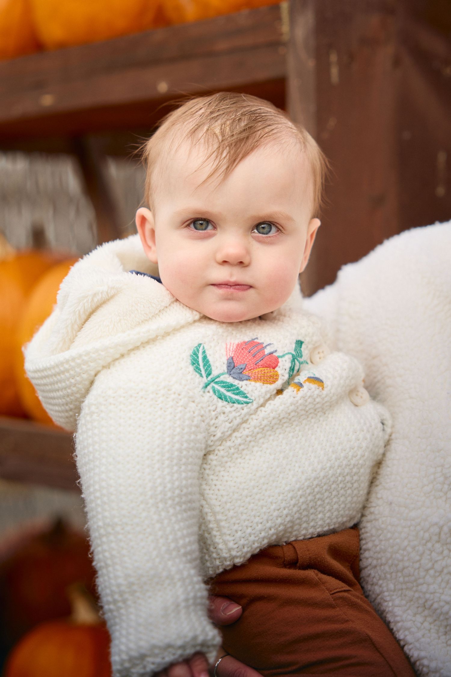 Close-up portrait of baby wearing cream knit sweater with floral embroidery.