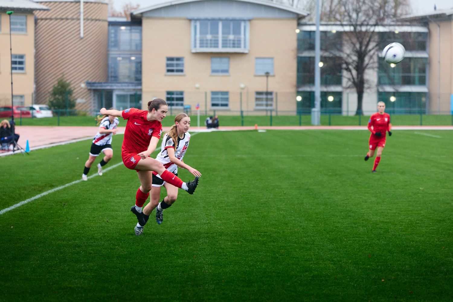 Soccer players compete on a bright green artificial turf field during a match at a school sports facility.