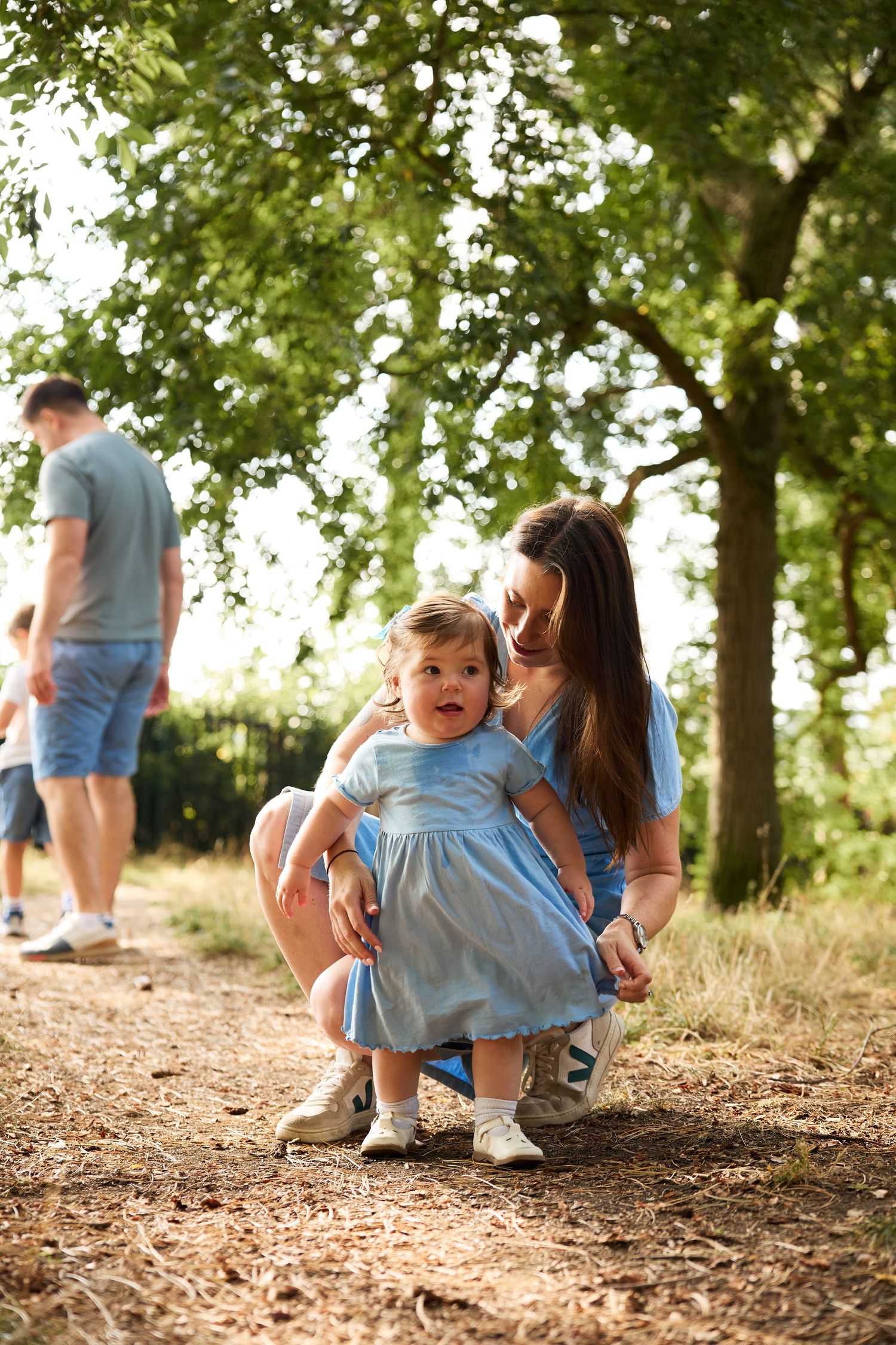 Candid family moments captured on a dirt path through a sunlit wooded area.