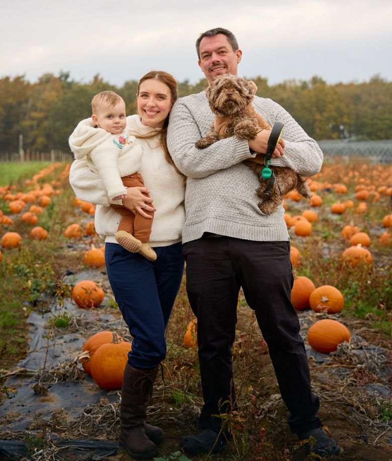 Family poses together in a pumpkin patch during autumn with their dog.