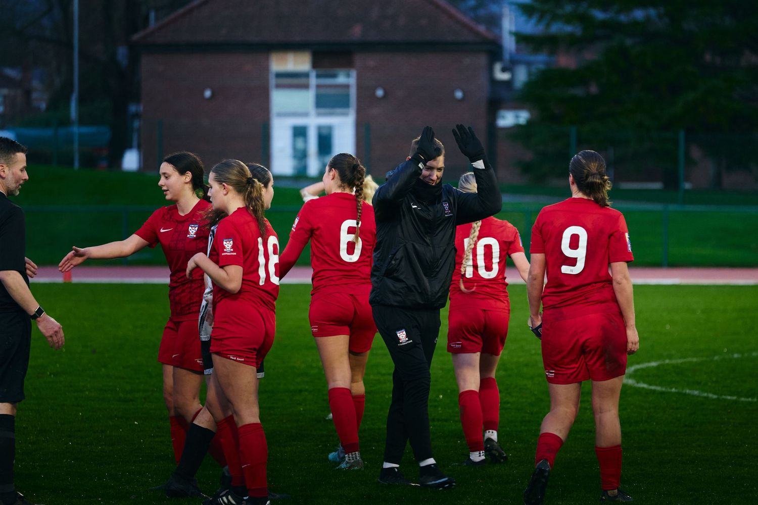 Soccer players in red uniforms gather on a grass field during practice or training session.