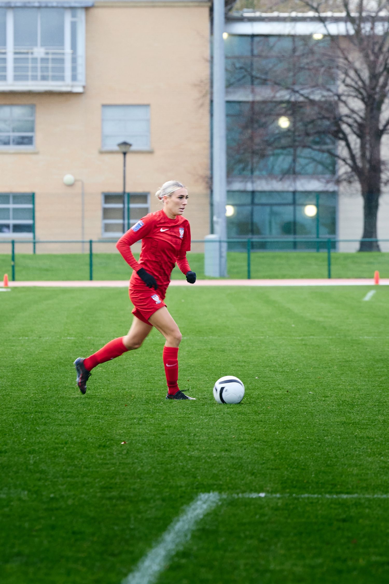 Soccer player in red jersey dribbles ball across green grass field during practice session.